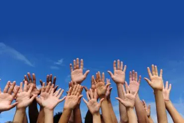 A group of hands raised together against a clear blue sky